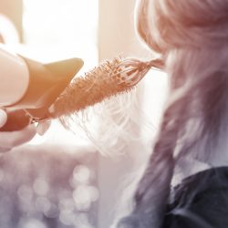 Hairdresser's hands holding hair dryer and drying client hair in beauty salon,